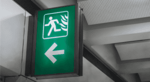 Green emergency exit sign with a running figure and left arrow, representing emergency preparedness, evacuation planning, and business continuity.