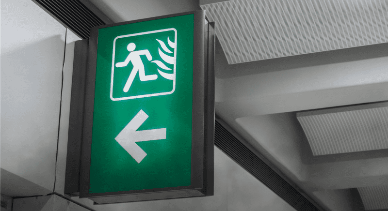 Green emergency exit sign with a running figure and left arrow, representing emergency preparedness, evacuation planning, and business continuity.